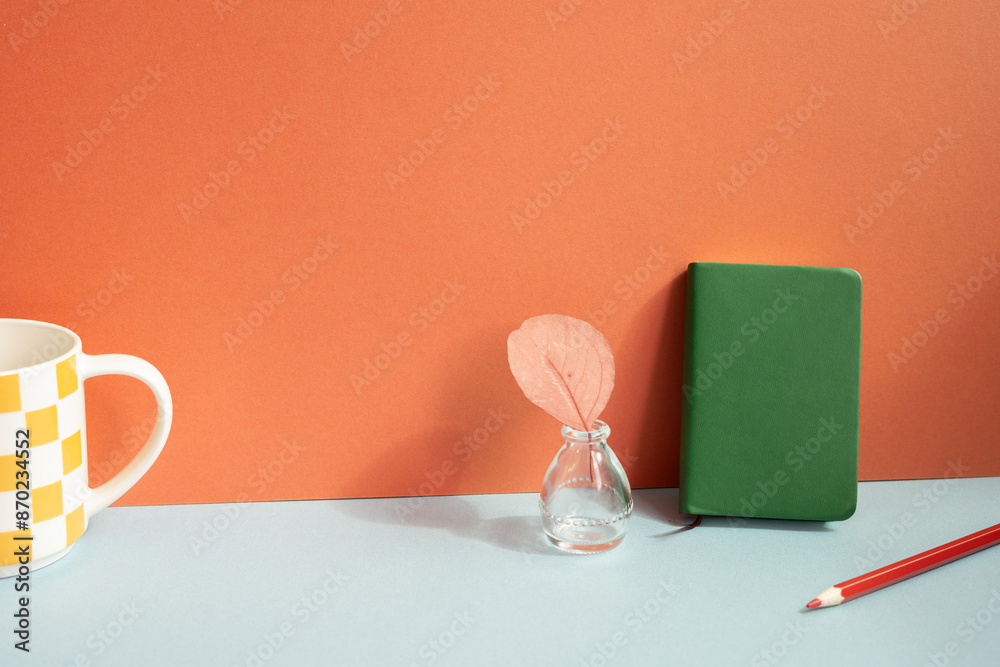 Workspace object. Notebook, colored pencil, vase of plant, mug cup on gray desk. red wall background