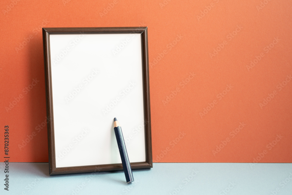 Empty photo frame with colored pencil on gray shelf. red wall background