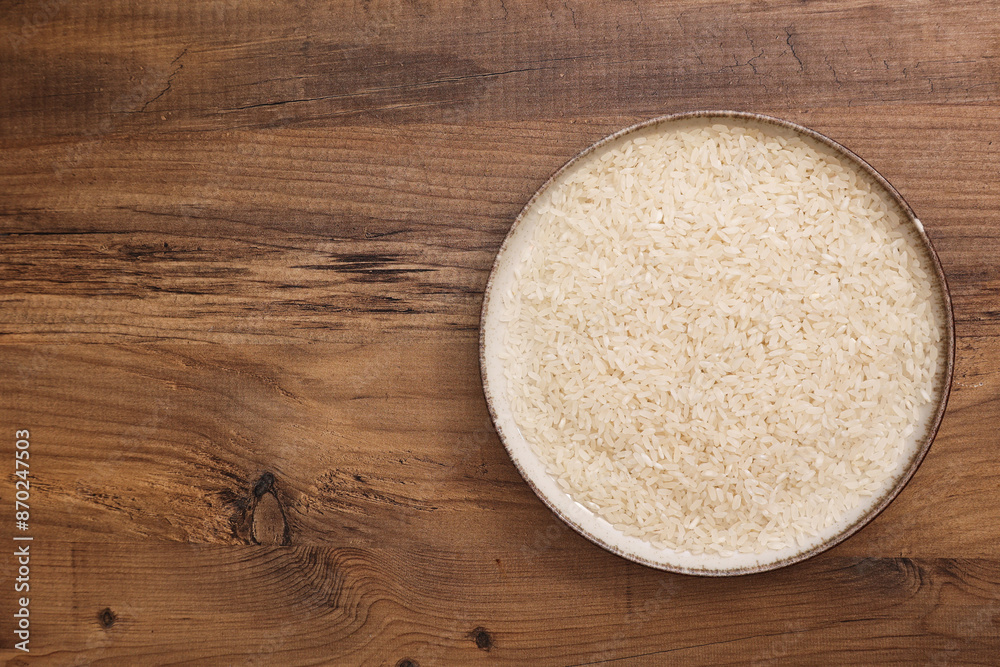 Top view of a bowl filled with rice on a wooden table, showcasing the grain's texture and natural color. Top view of a bowl filled with rice on a wooden table, showcasing the grain's texture and natural color.