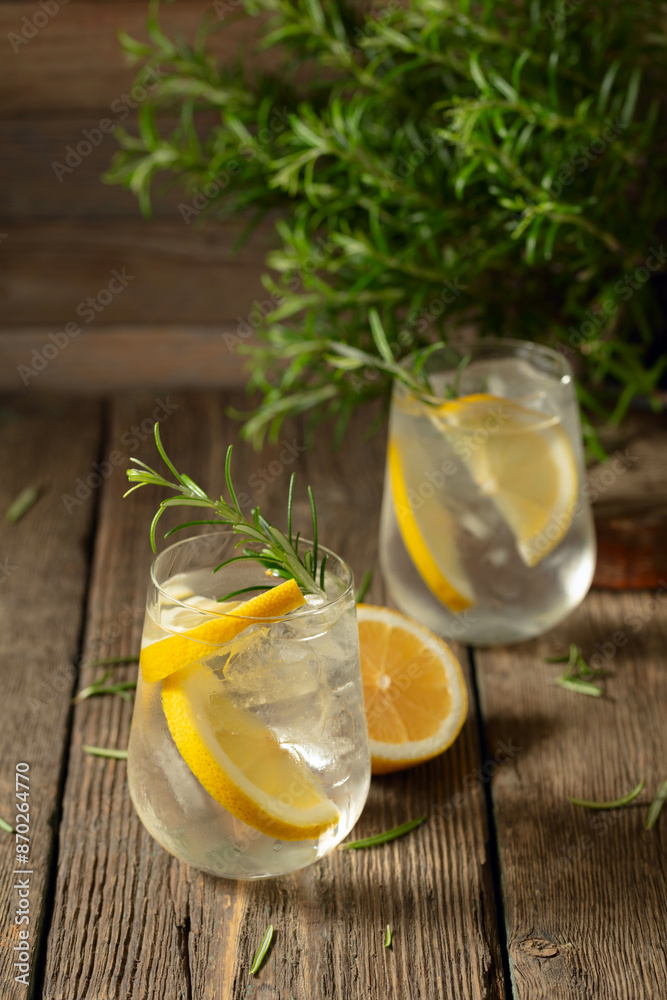 Fototapeta premium Cocktail gin tonic with ice, lemon, and rosemary on a old wooden table.
