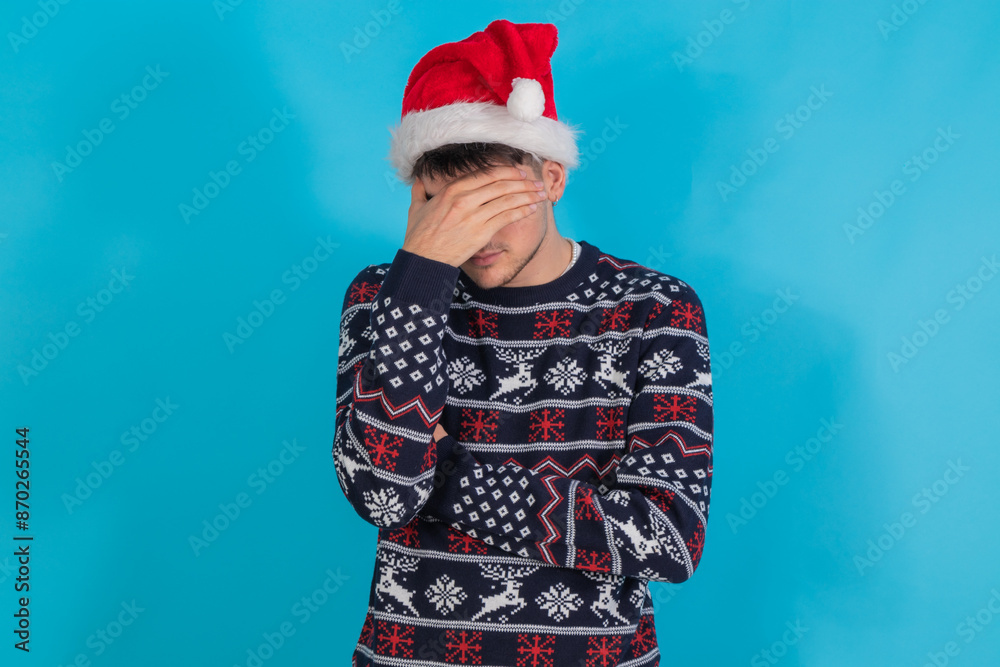 isolated young man with christmas sweater and santa claus hat sad or overwhelmed expression isolated young man with christmas sweater and santa claus hat sad or overwhelmed expression