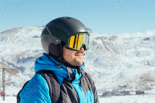 Skier standing on a slope. Man in a blue suit, the helmet and mask in skiing is to ski. In the background snow-capped mountains © Alina