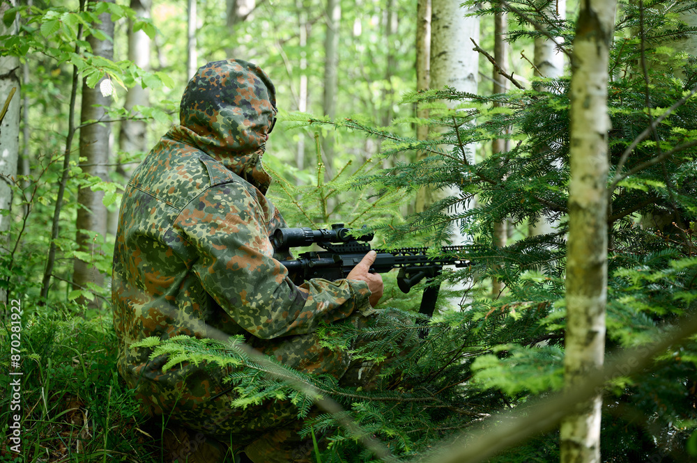 Hunter with rifle wearing camouflage suit sitting in ambush. Camouflaged sniper in the forest in ambush. Military man hide in the woods with rifle. Hunter with rifle wearing camouflage suit sitting in ambush. Camouflaged sniper in the forest in ambush. Military man hide in the woods with rifle.