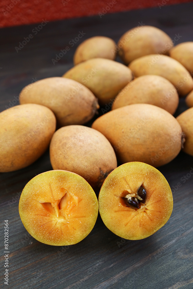 Closeup of Cut Sapodilla Fruit with Heap of Whole Fruits in the Backdrop Closeup of Cut Sapodilla Fruit with Heap of Whole Fruits in the Backdrop