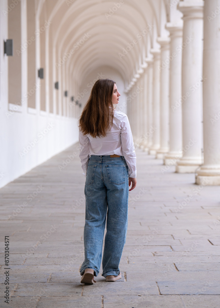 Full length rear view of a brunette. A stylish young woman with long hair walks among white columns Full length rear view of a brunette. A stylish young woman with long hair walks among white columns