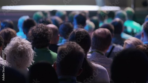 Large audience listening attentively to a speaker at a tech conference. Capturing the focused atmosphere in a dimly lit venue.