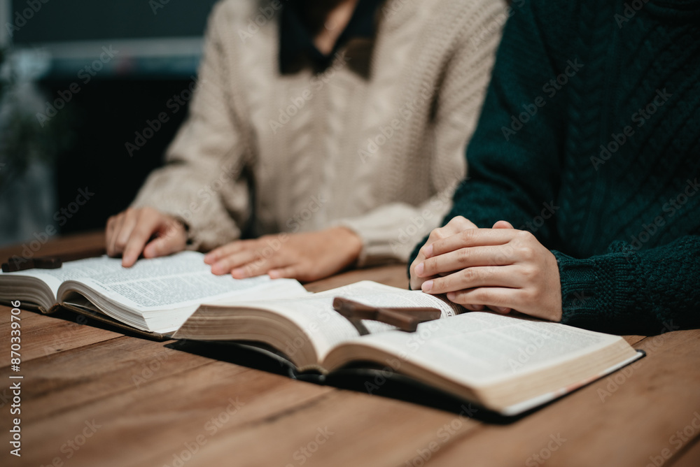 Group of Christians sit together and pray around a wooden table with blurred open Bible pages in their homeroom. Group of Christians sit together and pray around a wooden table with blurred open Bible pages in their homeroom.
