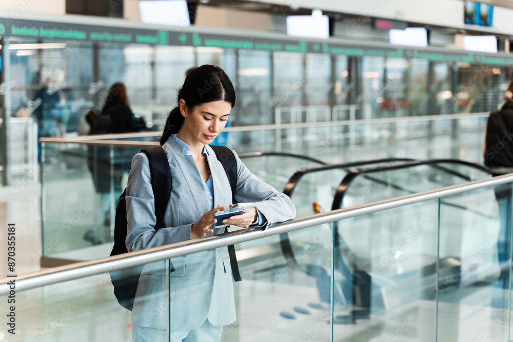 Traveler standing with documents near escalator in airport terminal and waiting for flight departure to start 2024 summer vacation. Woman looking in smartphone in airport lobby Traveler standing with documents near escalator in airport terminal and waiting for flight departure to start 2024 summer vacation. Woman looking in smartphone in airport lobby