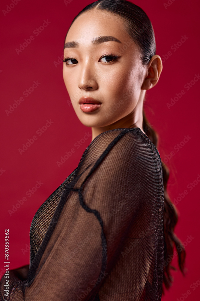 Fashion asian woman in black sheer top posing on red background with eyes closed and hands on hips Fashion asian woman in black sheer top posing on red background with eyes closed and hands on hips
