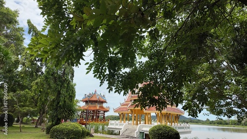 Park with trees, bushes and lawn. A lake, an Asian-style pavilion and hills.