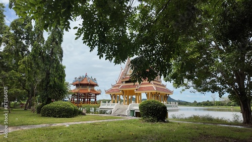 Park with trees, bushes and lawn. A lake, an Asian-style pavilion and hills.