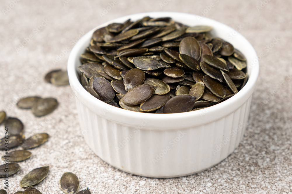 Peeled pumpkin seeds in plate on gray stone background, close-up Peeled pumpkin seeds in plate on gray stone background, close-up