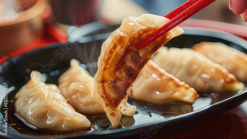 Close-up of chopsticks picking up delicious pan-fried gyoza dumplings with savory dipping sauce, Asian cuisine