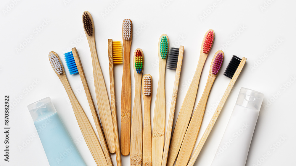 Obraz premium Top view of eco-friendly bamboo toothbrushes with colorful bristles and toothpaste tube on white background, Natural organic bathroom beauty product concept, dental hygiene, minimal flat lay