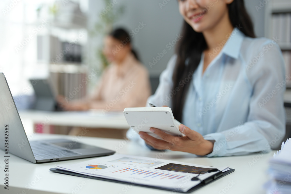 Asian businesswoman works on laptop and calculates with financial calculator from graphs, statistics, charts. Planning. Business success results in modern office. Asian businesswoman works on laptop and calculates with financial calculator from graphs, statistics, charts. Planning. Business success results in modern office.