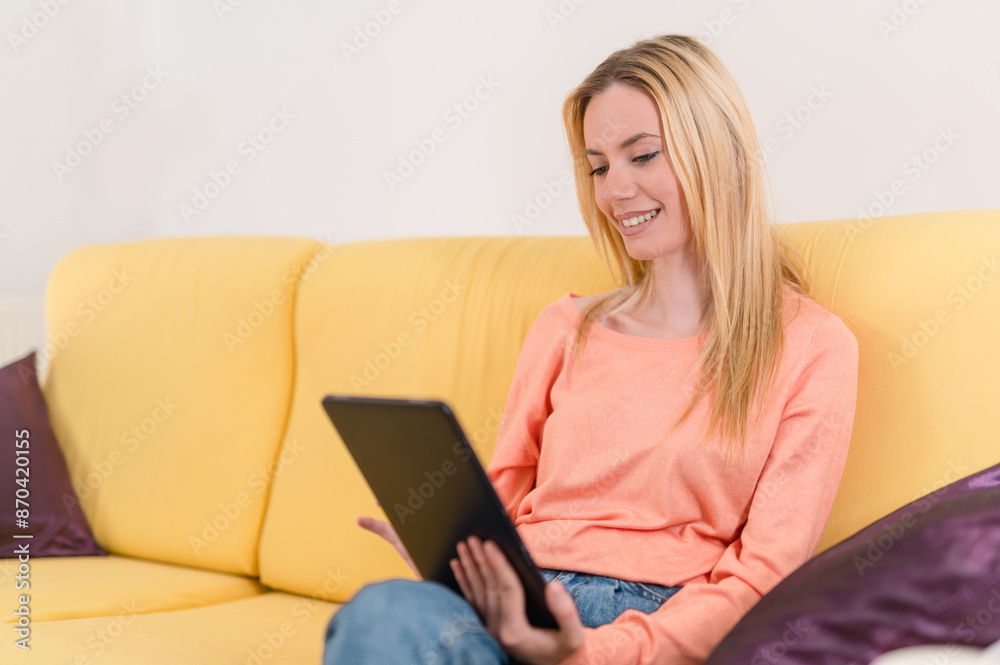 Blonde attractive girl relaxing on sofa in her apartment and holding a tablet Blonde attractive girl relaxing on sofa in her apartment and holding a tablet