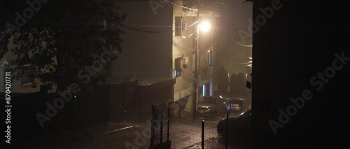 Heavy rain on the street in Eastern Europe. Night, lightning, one lantern is burning near a brick house. Anamorphic lens