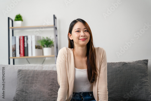 A portrait of beautiful young asian woman is sitting on a couch and smiling.