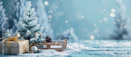 Festive winter items like a decorative sled, fir tree, and gift box against a soft, blue backdrop symbolize the holiday season, providing space for text or images. Copy space image photo