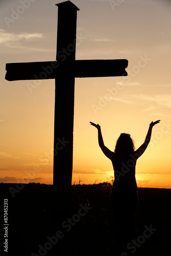 Woman praying at sunset. Shilouette with a cross. France.