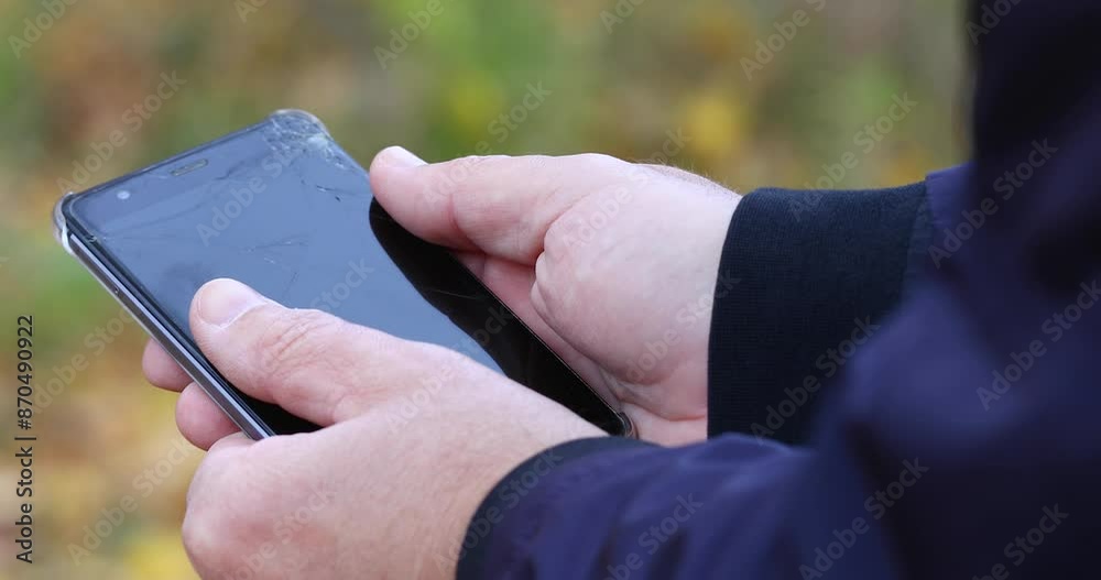 A man on the street holds a broken phone with cracks on the screen A man on the street holds a broken phone with cracks on the screen