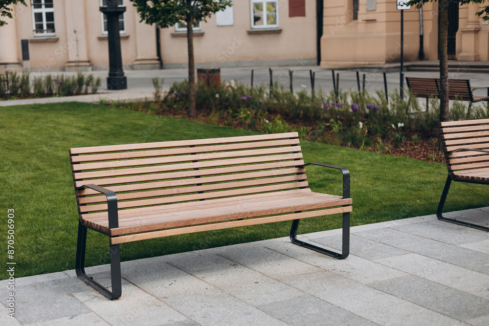 A modern wooden bench standing in the park by the sidewalk. Comfortable bench in recreation area. City improvement, urban planning, public spaces. A modern wooden bench standing in the park by the sidewalk. Comfortable bench in recreation area. City improvement, urban planning, public spaces.