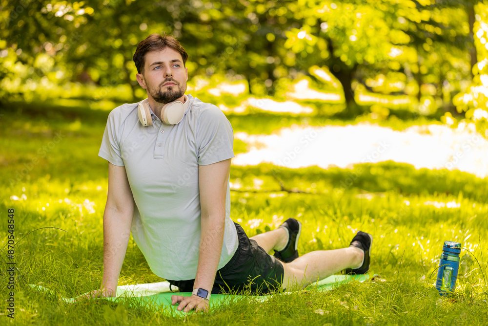 Fit flexible man doing workout yoga stretching on a sports mat in park. Raising head. Young male guy enjoying exercising outdoors. Active sportsman motivation. Determined athlete healthy lifestyle.