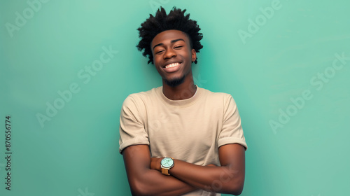A joyful millennial man with a confident smile, wearing a watch, posing with folded arms against a solid green background