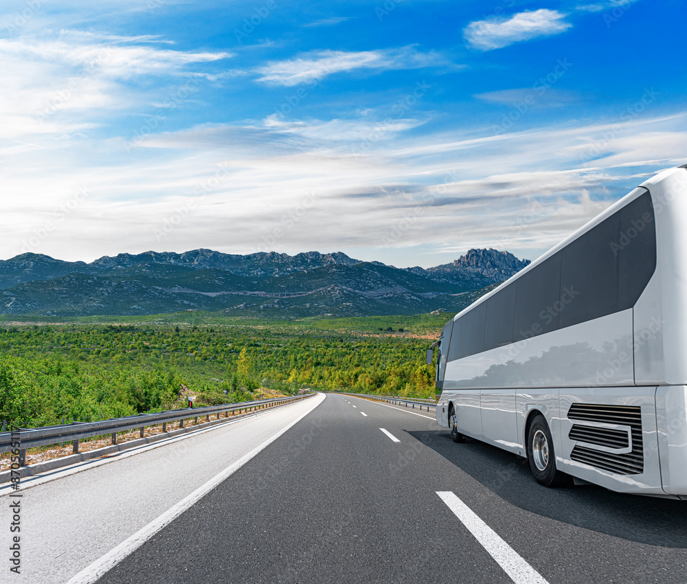A white tourist bus travels along a picturesque mountain road.