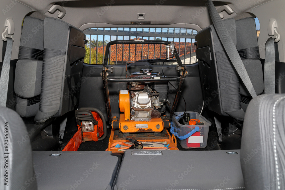 Fototapeta premium Hired (rented) plate compactor and chainsaw for do it yourself (DIY) jobs at home, i.e., cut, fell tree and lay pavers. Equipment transported in family car (SUV), with seats down.