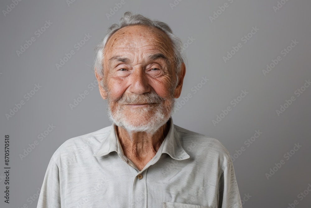Happy older man in shirt smiling at camera on gray background.