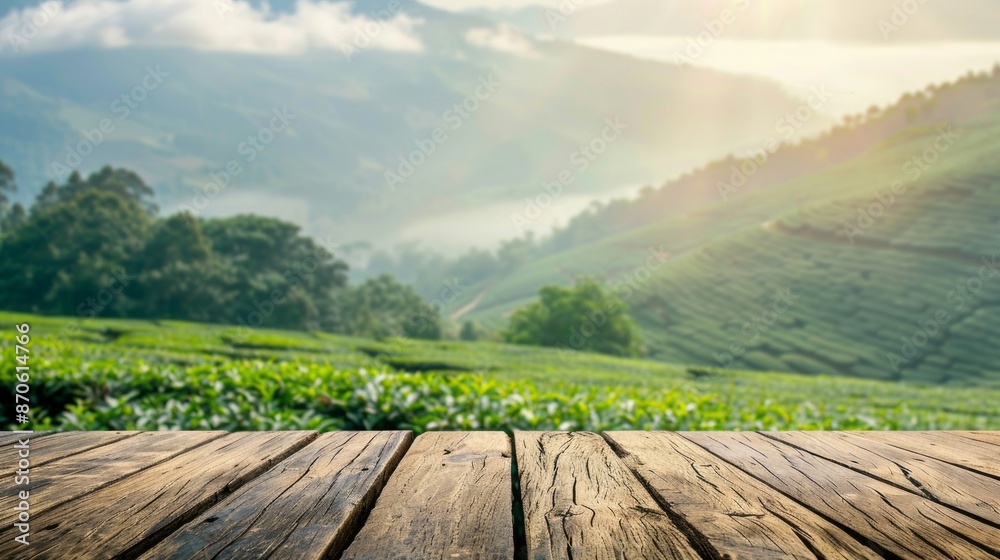 In the forefront, a wooden tabletop overlooks a lush green tea plantation in rolling hills. The morning mist is pierced by sunlight, setting a serene tone In the forefront, a wooden tabletop overlooks a lush green tea plantation in rolling hills. The morning mist is pierced by sunlight, setting a serene tone
