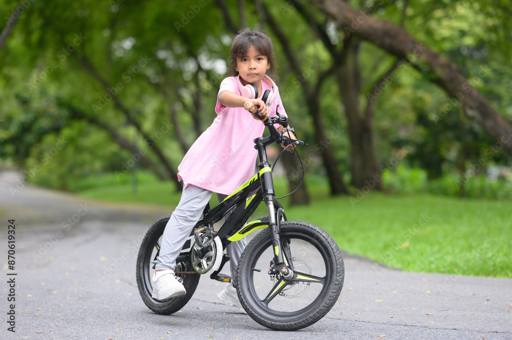 Young Asian girl rides her bicycle with happiness.In the park, natural background Young Asian girl rides her bicycle with happiness.In the park, natural background