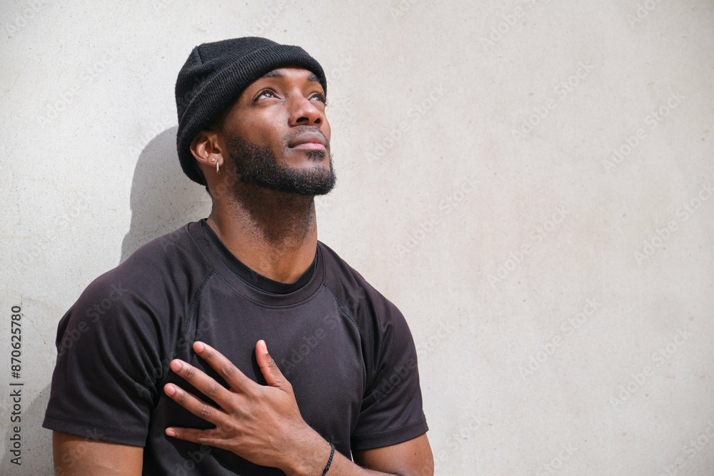 Young black man standing with hand over heart while looking up with hope