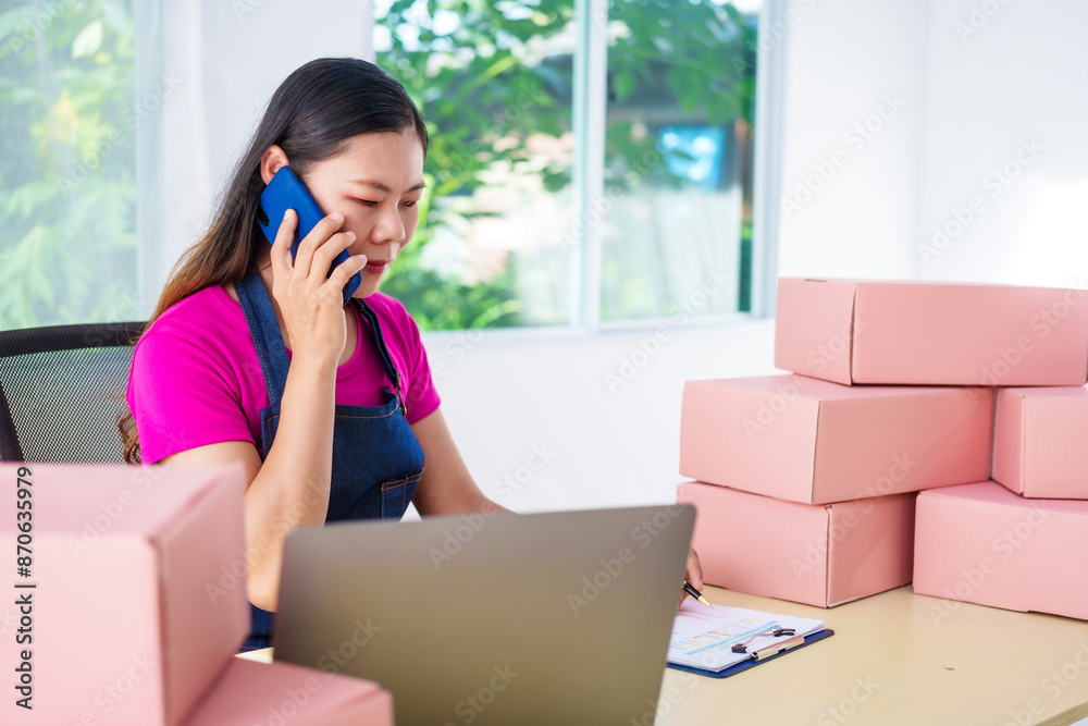 A woman in overalls sells products online, inspects parcels, takes customer orders, works at a desk, and uses pink boxes to pack items ready for shipping to customers. A woman in overalls sells products online, inspects parcels, takes customer orders, works at a desk, and uses pink boxes to pack items ready for shipping to customers.
