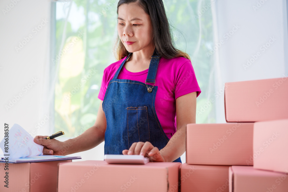 A woman in overalls sells products online, inspects parcels, takes customer orders, works at a desk, and uses pink boxes to pack items ready for shipping to customers. A woman in overalls sells products online, inspects parcels, takes customer orders, works at a desk, and uses pink boxes to pack items ready for shipping to customers.