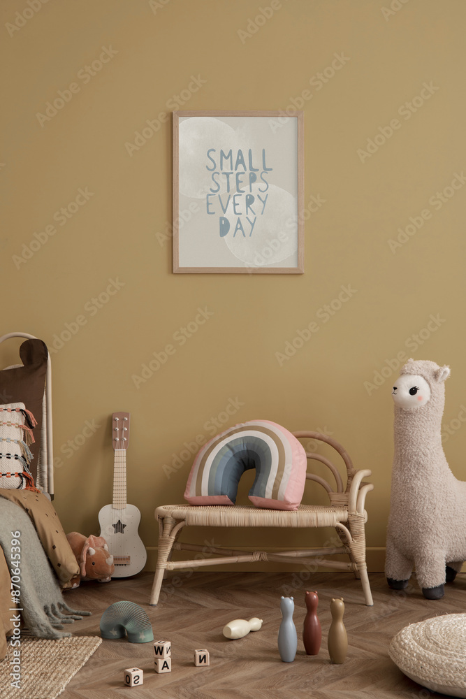 Obraz premium Warm and cozy kid room interior with mock up poster frame, yellow wall, braided armchair, plush toys, wooden block toys, plaid, guitar, pouf, cup and personal accessories. Home decor. Template.