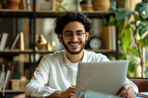 Portrait of young Arab man using laptop and notebook.