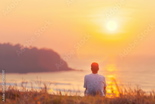 A man sits on a grassy hill overlooking the ocean