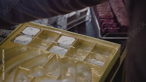 A chocolatier placing white shiny gelatin-coated chocolate with writings inside a chocolate box. photo