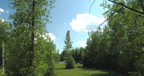 Drone shot moving at low angle between the trees in a public park, in summer