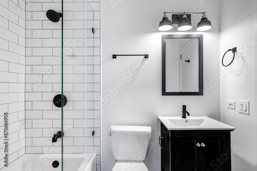A small modern bathroom with a dark vanity, mirror frame, and hardware. White subway tiles line the bathtub and shower with black faucets.