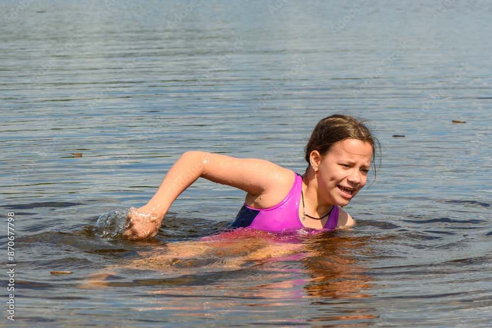 A teenage girl in a blue swimsuit enjoys swimming in the warm calm lake water A teenage girl in a blue swimsuit enjoys swimming in the warm calm lake water