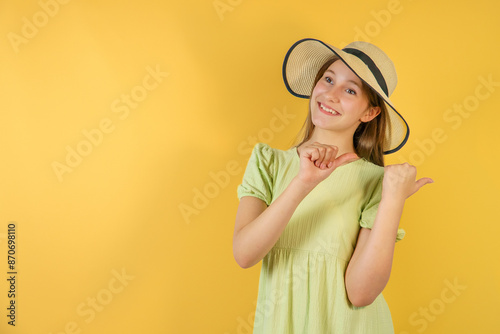 cheerful little girl wears a straw hat. beach fashion for children. small child on a yellow background shows a thumbs up gesture. a holiday of joy and activity. long-awaited summer holidays