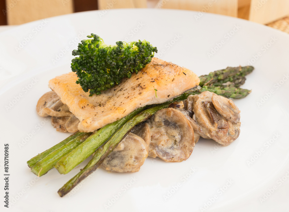 Dish of fried river trout fillet with garnish of broccoli, asparagus sprouts and mushroom sauce on white background Dish of fried river trout fillet with garnish of broccoli, asparagus sprouts and mushroom sauce on white background