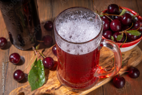 Craft cherry beer or cider alcohol drink mug and bottle on wooden table with fresh ripe cherries, copy space