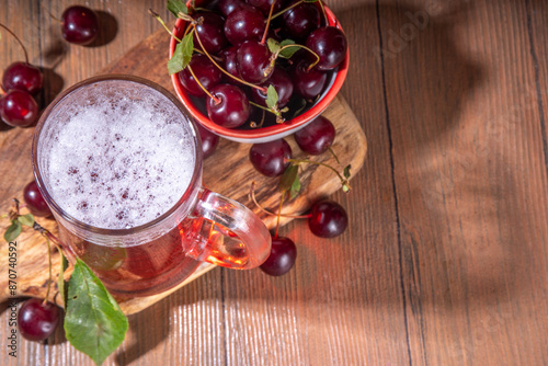 Craft cherry beer or cider alcohol drink mug and bottle on wooden table with fresh ripe cherries, copy space