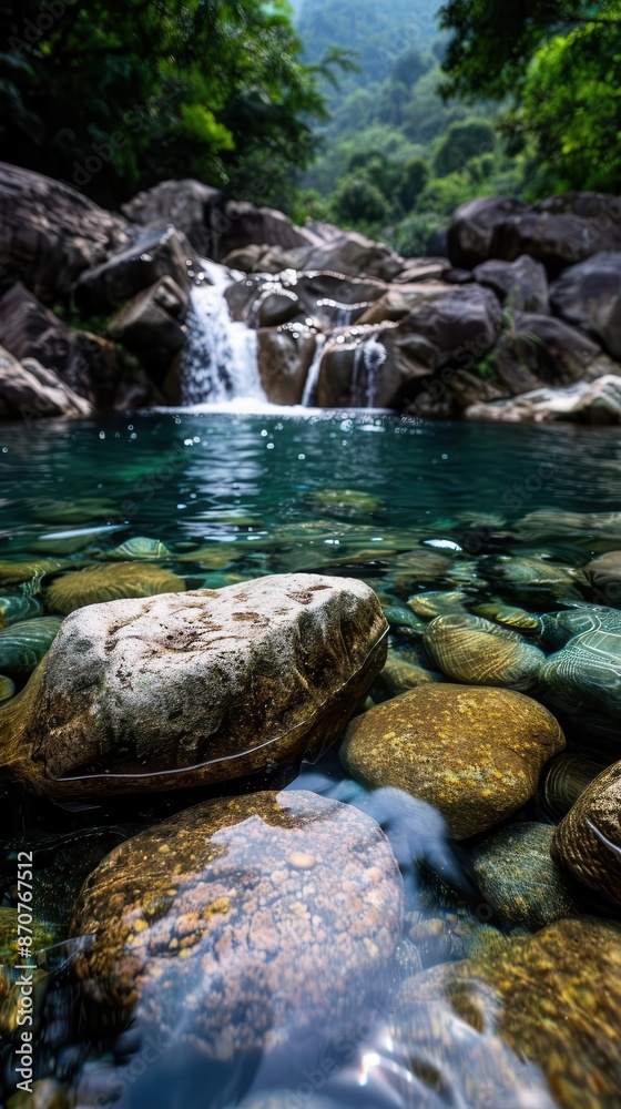 Fototapeta premium Crystal clear waterfall cascading over rocks into a pristine pool, surrounded by lush greenery, perfect for illustrating natural beauty and serene landscapes