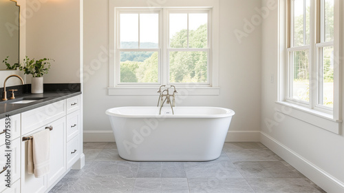 A serene bathroom with a bathtub, surrounded by modern fixtures and a large window offering a view of lush greenery. © NaphakStudio