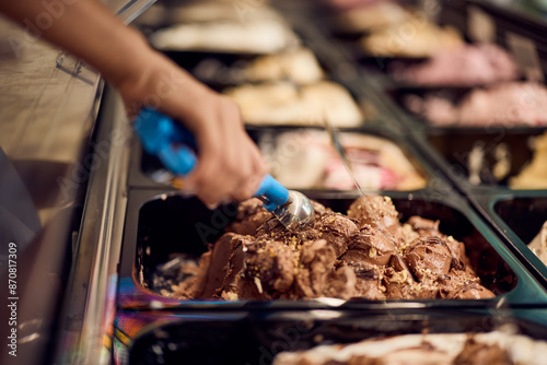 Chocolate ice cream in a container in a glass case, using a scoop of it. photo